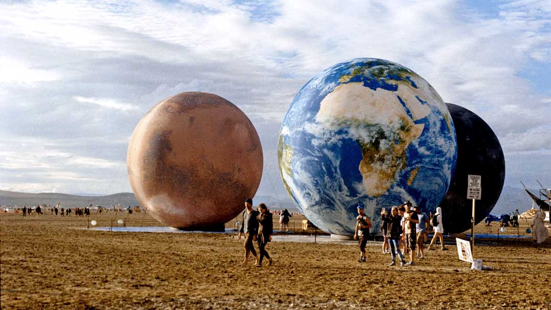 Burning Man Festival goers walk by a display of giant inflatable planets of our solar system